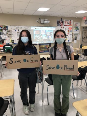 Environmental club members India Campomanes and Sage Campomanes holding their environmentally friendly recycled cardboard signs. 