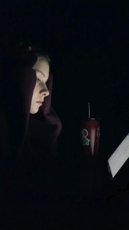 Student Charlie Tellier looks at a computer screen in a dark room doing homework.
