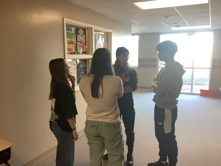 Ulric Pierce, Nia Pedrett, Susan Campie, and Brian Kim discuss the Rock-Paper-Scissors Tournament in the lower D-wing hallway, on April 6th, with 8 days left before the tournament.