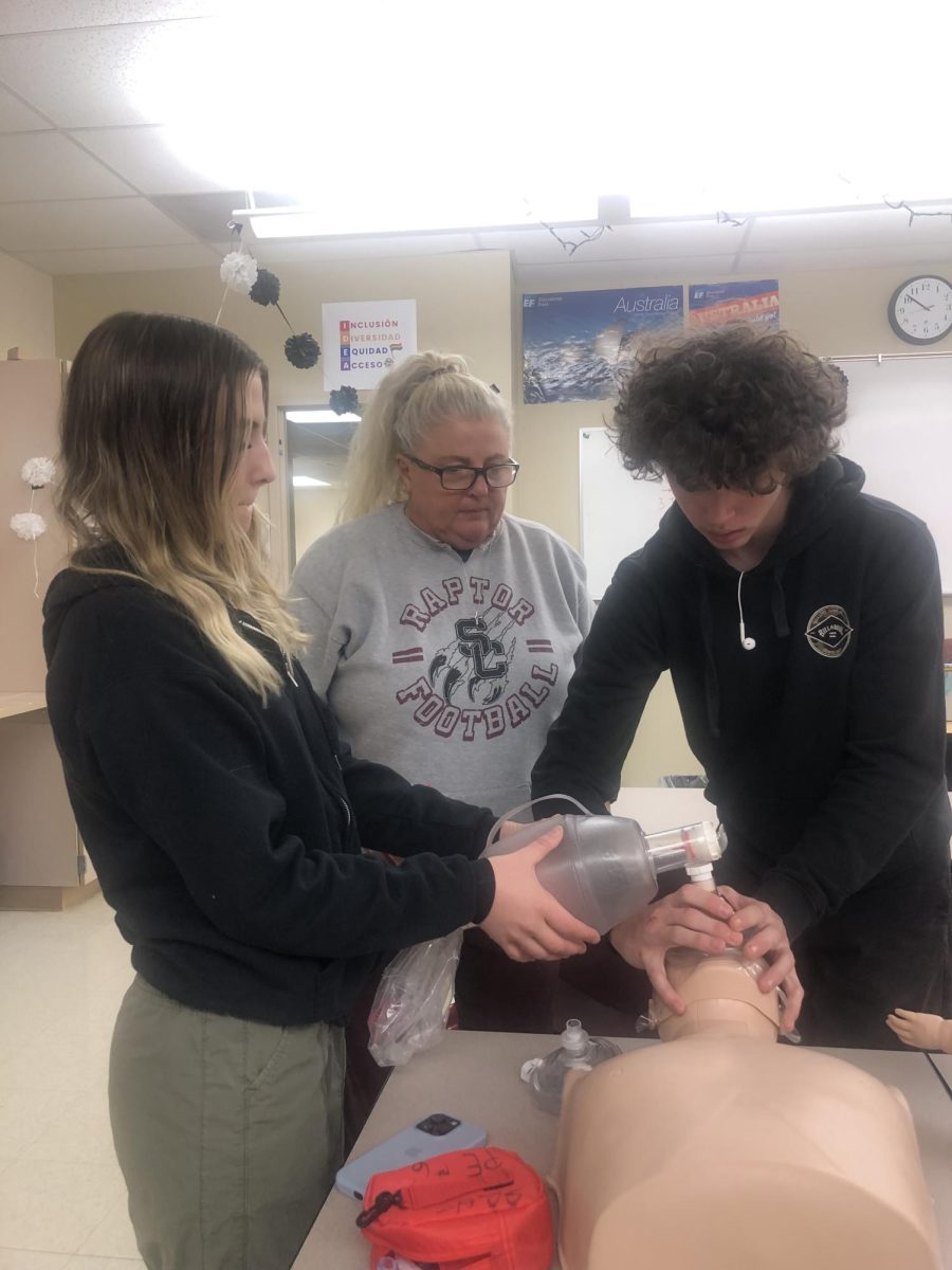 Sara Whitely, a PE teacher and coach at Silver Creek teaches Secorra Heinrichs, Senior, and Casey Allin, Sophomore, how to deliver deep ventilations to the CPR dummy