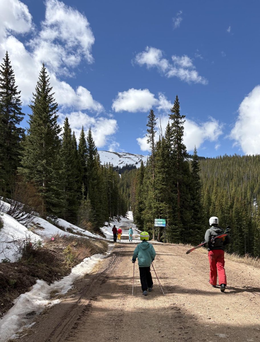 A group of skiers walk on a dirt road surrounded by trees.